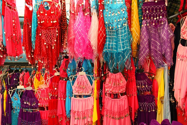 An image showcasing a belly dancer gracefully twirling vibrant silk veils, while captivatingly playing finger cymbals, as they are surrounded by an array of mesmerizing, intricately designed tambourines and zills