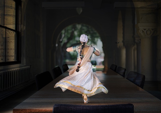 An image showcasing a graceful Indian dancer in vibrant traditional attire, gracefully moving her hips and hands while adorned with intricate jewelry, against a backdrop of a majestic Indian temple