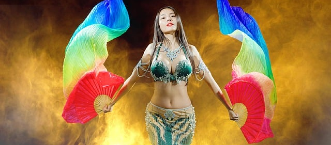 An image capturing the essence of belly dance classes: vibrant, swirling movements, gracefully arched bodies, and the rhythmic jingle of hip scarves, revealing the captivating realities of this ancient art form